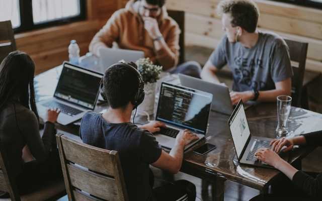 Members of a small agency team working together around a laptop in an open-plan office, reviewing work on screen.